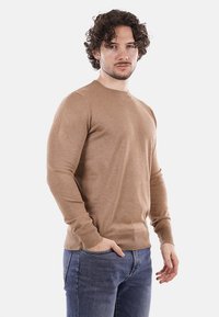 Maglione leggero marrone in un design aderente, realizzato in tessuto morbido, con collo a giro e maniche lunghe, abbinato a jeans blu.