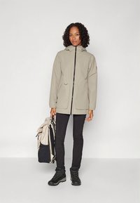 Light gray waterproof jacket with a hood, front zip, and pockets, paired with black pants and sturdy black hiking boots.