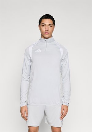 Hellgraues athletisches Shirt mit einem halben Reißverschluss am Kragen, langen Ärmeln und weißen Akzenten an den Schultern, gefertigt aus einem glatten, atmungsaktiven Material.