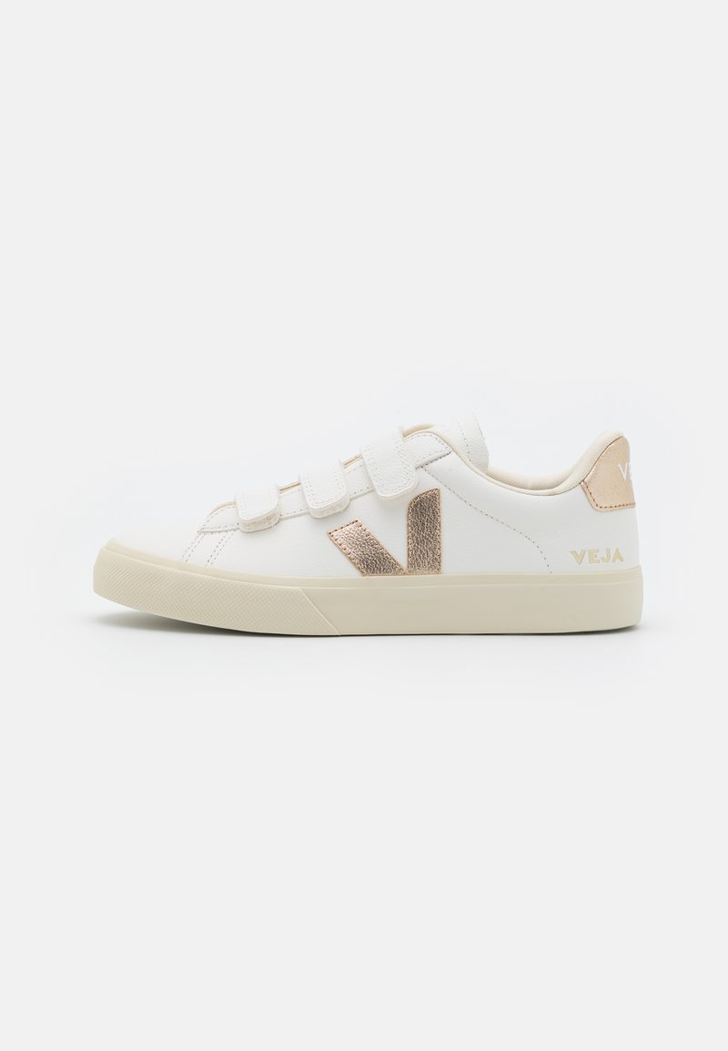Zapatilla blanca con correas de velcro, acentos beige, logo 'V' texturizado en dorado y suela de goma crema. Parte superior de cuero suave.