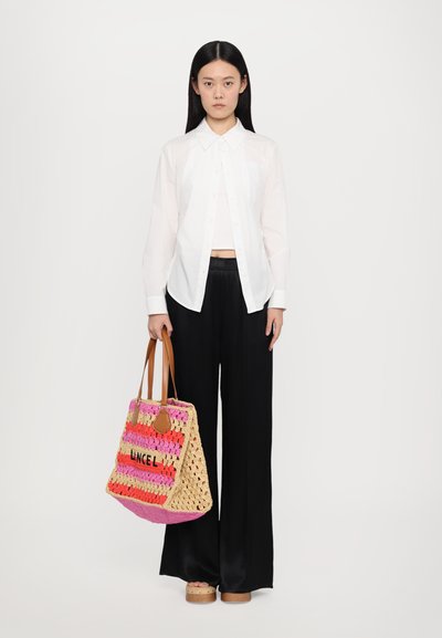 Sac en crochet avec des rayures rose, orange et crème, orné de détails en cuir beige. Un mannequin portant une chemise blanche et un pantalon noir se tient à côté.