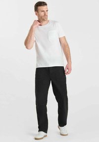 Witte katoenen t-shirt met een borstzak, gecombineerd met losse zwarte cargo-broek en witte sneakers met beige zolen.