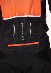 Svart och orange cykeltröja i ett mjukt, ventilerande material. På baksidan finns reflekterande ränder och "ENDURANCE"-logotyp.