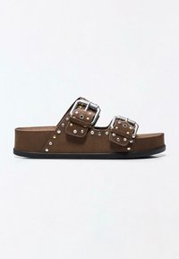 Sandale mule en daim marron avec deux brides argentées à boucle et détails à clous métalliques, équipée d'une légère semelle plateforme et d'une semelle extérieure noire.