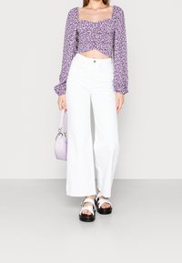 Fialový květinový top na krátký rukáv s dlouhými, nafouklými rukávy; bílé kalhoty s širokými nohavicemi; černé sandály na platformě s bílými popruhy; levandulová kabelka.