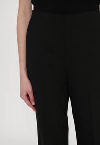 Čierne upravené nohavice s hladkou textúrou, so strihom rovného nohu a bočnými vreckami, nosené s čiernym rebrovaným topom.