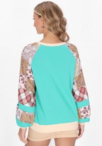 Top in cotone verde menta con maniche lunghe decorate da motivi paisley, a quadri e floreali. Collo e vita a coste.