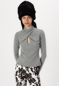 Gray long-sleeve top with a draped neckline and keyhole detail, paired with black-and-white cow print pants. Black faux fur hat.