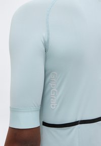 Close-up of a light blue short-sleeve cycling jersey sleeve featuring the GripGrab logo and a black horizontal stripe on the back.