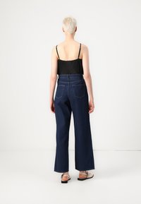 Σκοτεινές τζιν παντελόνες με φαρδύ πόδι και ψηλή μέση, με δύο πίσω τσέπες, συνδυασμένες με μία μαύρη πλι�σέ τοπ καμισόλ.