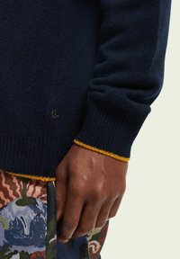 Marine gebreide trui met gele accenten bij de manchetten; intricate textuur stof; gecombineerd met geprinte broek met bloemrijke en abstracte ontwerpen.