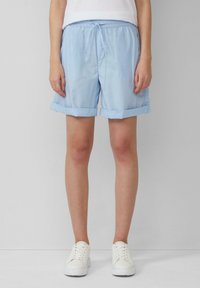 Shorts bleu clair, avec une taille élastique et un cordon de serrage, présentant des revers et un tissu lisse et léger. Associés à des baskets blanches.