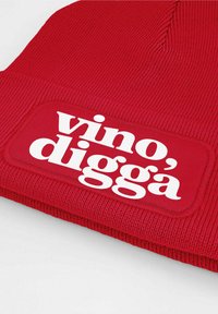 Red knitted beanie with a textured finish. Features a prominent white patch displaying the text "vino', diggà" in bold font.