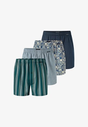Mannelijke zonder shirt die naar beneden kijkt, draagt blauwgroen gestreepte boxershorts met elastische tailleband tegen een effen witte achtergrond.
