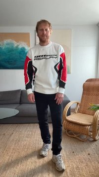 Sweatshirt branca com detalhes em vermelho e preto, apresentando o texto "981sports REPLAY"; combinado com jeans skinny pretos e sapatilhas cinzas.