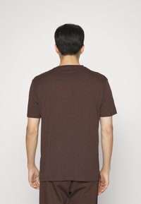 Hnědé bavlněné tričko s krátkými rukávy a kulatým výstřihem, s jednobarevným zadním designem. Měkká textura a volný střih.