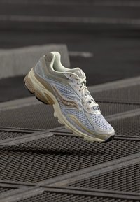 Weißer und hellgrauer Sportschuh mit einem Mesh-Obermaterial, gepolstertem Kragen, strukturiertem Sohle und subtilen beigefarbenen Akzenten.