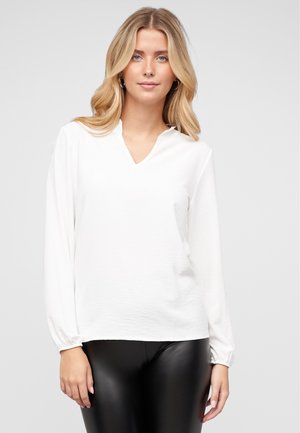 Witte blouse met lange mouwen en een V-hals, voorzien van geplooide manchetten en een gestructureerde stof. Draagt met zwarte leren look broek.