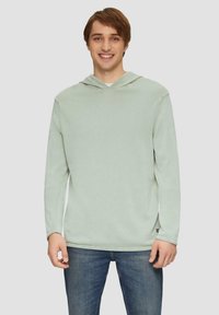 Lichtgroene hoodie gemaakt van zachte stof. Heeft lange mouwen, een ruime capuchon en een relaxte fit. Gedeeltelijk gedragen met blauwe spijkerbroeken.