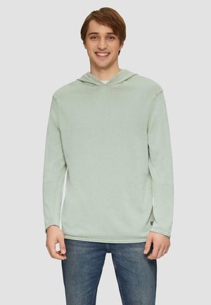 Lichtgroene hoodie gemaakt van zachte stof. Heeft lange mouwen, een ruime capuchon en een relaxte fit. Gedeeltelijk gedragen met blauwe spijkerbroeken.