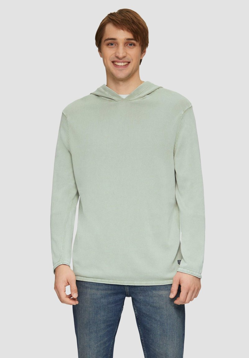 Lichtgroene hoodie gemaakt van zachte stof. Heeft lange mouwen, een ruime capuchon en een relaxte fit. Gedeeltelijk gedragen met blauwe spijkerbroeken.
