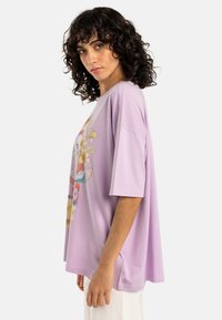 Tricou oversized lavandă din bumbac, cu un print grafic colorat cu flori pe partea din față și un design lejer cu umeri căzuți.