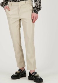 Beige, slim-fit broek van faux leder met zijzakken en een voorplichaam. Gecombineerd met zwarte instappers met een gouden kettingaccent.