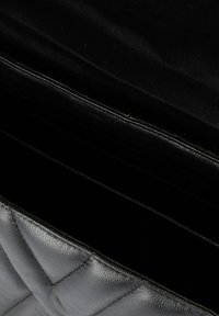 Interior de un bolso de mano de cuero negro acolchado con múltiples compartimentos, con una superficie texturizada y un forro suave y oscuro.