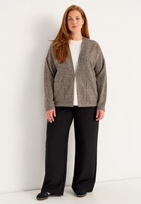 Grå texturerad cardigan med öppen fram, två fickor, tillsammans med svarta vida byxor och svarta slip-on skor. Enkel vit skjorta under.