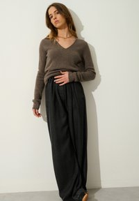 Brun v-ringad tröja i mjukt material, som kombineras med högmidjade svarta veckade vida byxor, designade för en avslappnad passform.