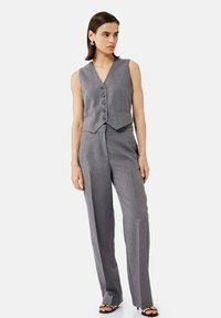 Gilet grigio su misura con sei bottoni e taglio slim, abbinato a pantaloni a vita alta e gamba larga coordinati. Tessuto liscio, senza motivi visibili.