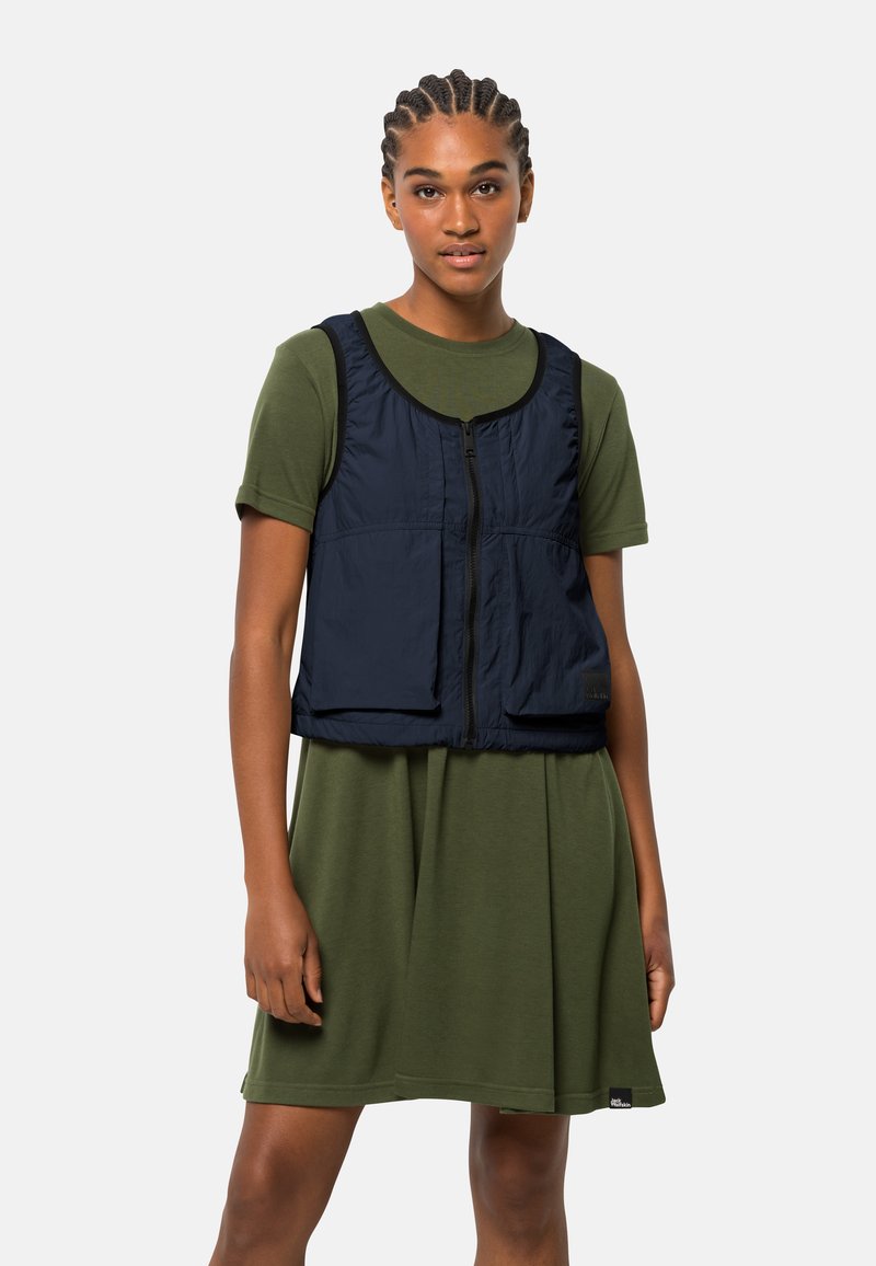 Niebieska kamizelka z zamkiem błyskawicznym, wykonana z lekkiego materiału, z dwiema przednimi kieszeniami, nałożona na zieloną sukienkę z krótkim rękawem. Gładka tekstura i swobodny fason.