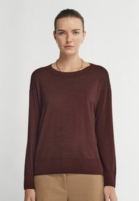 Maroon stickad tröja med rund halsringning, långa ärmar, ribbad nederkant och en avslappnad passform. Slät textur utan synliga mönster eller detaljer.