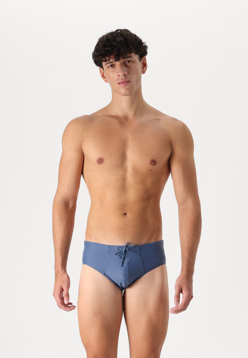 Blue swim briefs with a drawstring waist, made of smooth fabric; fitted design highlighting a streamlined shape.