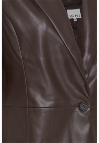 Blazer en similicuir marron foncé avec revers cranté, un bouton noir unique et étiquette de marque visible à l'intérieur du col.