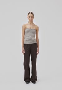 Top gris sin tirantes con una textura arrugada, combinado con pantalones marrones de pierna ancha. La modelo lleva zapatos negros, todo sobre un fondo neutro.