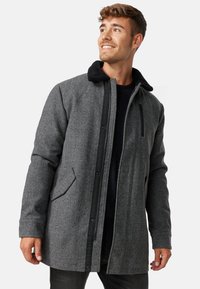 Abrigo de mezcla de lana gris con un cuello forrado de piel negra, cierre de cremallera y broches, bolsillos laterales y un ajuste holgado.