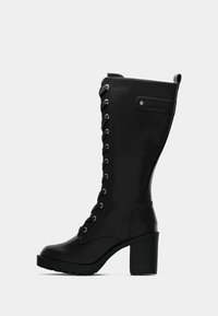 Černé kožené kotníkové boty do poloviny lýtek s předními šněrováním, blokovým podpatkem, robustní podrážkou a detailem postranního popruhu na bílém pozadí.