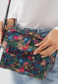 Borsa a tracolla floreale con sfondo scuro decorato con fiori e foglie colorate, hardware dorato e forma strutturata.