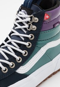 Vans höghöga sneakers med en marinblå canvasöverdel, teal- och lila detaljer, vit gummisula, metallöglor och kontrasterande vita snören.