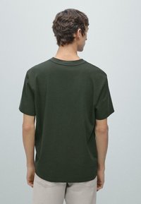 T-shirt a maniche corte con scollo rotondo in cotone verde scuro, caratterizzata da una vestibilità morbida e una texture liscia, vista da dietro.