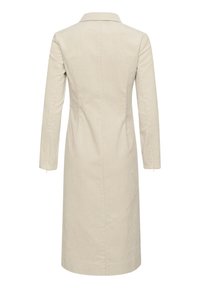 Robe en velours côtelé beige à manches longues, col, poches latérales et coupe droite, avec une texture côtelée verticale sur toute la surface.