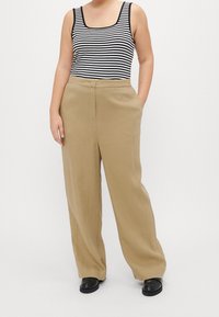 Pantaloni beige a gamba larga realizzati in un tessuto morbido, con una texture liscia, tasche frontali e una vita alta. Abbinati a un top senza maniche a righe.