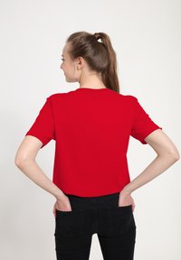 Red short-sleeve t-shirt with a round neckline, made of smooth fabric, viewed from the back. Worn with fitted black jeans.