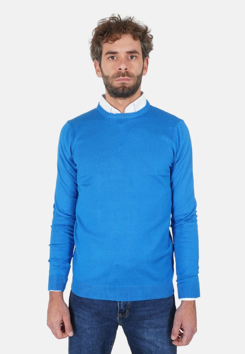 Maglione azzurro chiaro in maglia con scollo tondo e polsini a costine, indossato sopra una camicia bianca e abbinato a jeans blu scuro.