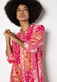 Lange, kleurrijke jurk met patchworkontwerpen in tinten roze en oranje. Zachte stof met bloempatronen en oprolbare mouwen.