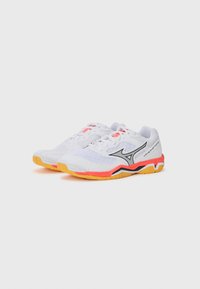 Baskets blanches de sport en matière mesh et synthétique, avec des accents orange et noir, une semelle texturée et un logo argenté.