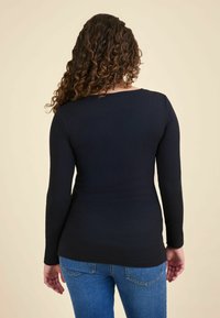 Tricou negru cu mâneci lungi, cu o textură ribbed și un guler rotund, purtat cu blugi albaștri. Vederea din spate arată o siluetă ajustată.