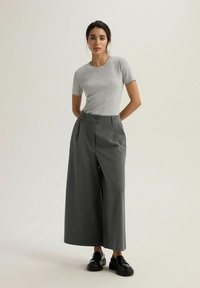 Szara koszulka z krótkim rękawem w połączeniu z szarymi spodniami o wysokim stanie i szerokiej nogawce, z zapięciem na guziki, noszona z czarnymi mokasynami.