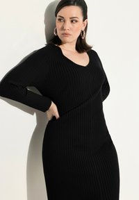 Schwarz geripptes Kleid mit langen Ärmeln und V-Ausschnitt, mit taillierter Passform und strukturiertem Stoff. Dezente seitliche Taschen.